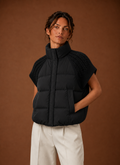 Women's black sleeveless puffer vest featuring stylish knit shoulder panels, perfect for layering in cool weather. 0